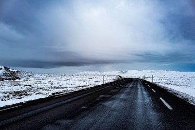 Road amidst snow covered field against cloudy sky