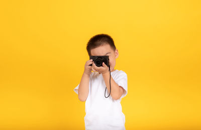 Portrait of young man photographing against yellow background