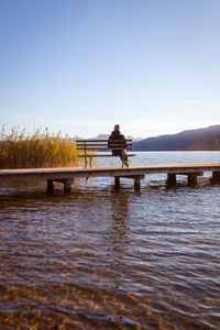 Man on pier over lake against clear sky