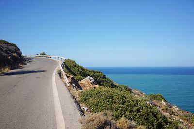 Panoramic view of road by sea against clear blue sky