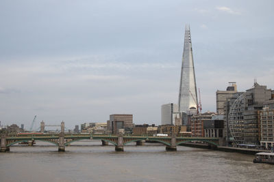 Bridge over river by buildings against sky in city