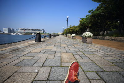 Footpath by street in city against clear blue sky