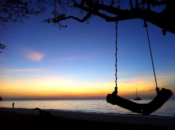 Silhouette swing hanging on tree against lake and sky at dusk