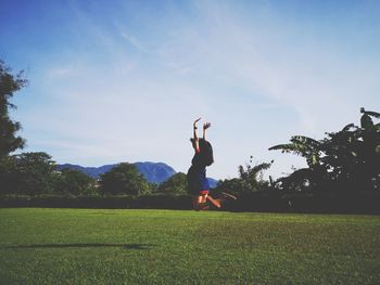 Woman with arms raised on field against sky