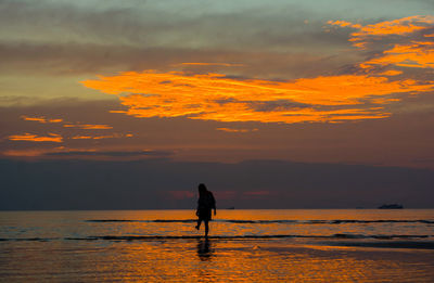 Silhouette man standing on beach against orange sky