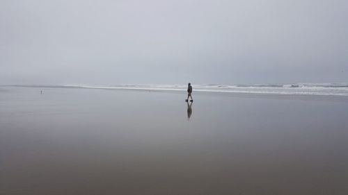 Distant view of man walking at beach against sky