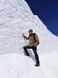 Full length of hiker standing by snow covered rock formation during sunny day