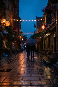 Rear view of people walking on wet street at night