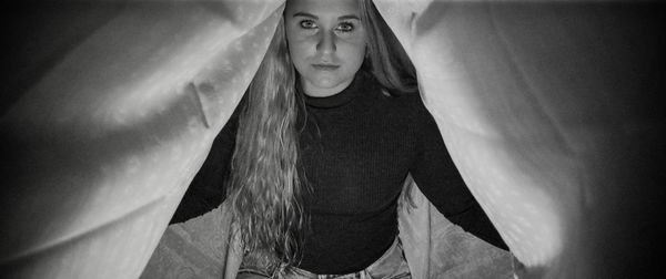 Portrait of young woman standing against curtain