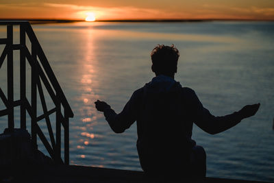 Rear view of silhouette boy standing at beach during sunset