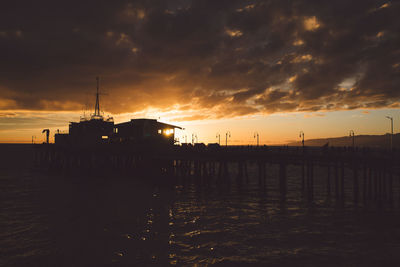 Silhouette santa monica pier over sea against cloudy sky during sunset