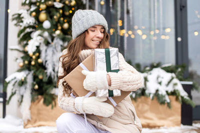 A cute girl in mittens has closed her eyes and is enjoying gifts on the street in winter in the city