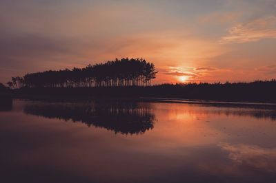 Silhouette trees by lake against sky during sunset