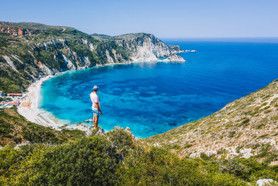 Man standing on rock by sea against sky