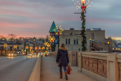 Rear view of woman walking on illuminated buildings in city against sky