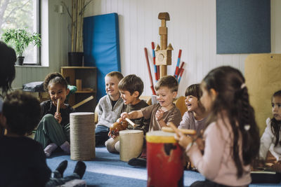 Happy multiracial male and female students enjoying while playing drum kit in child care center