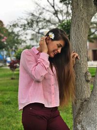 Smiling woman standing by tree trunk