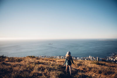 Rear view of woman standing on sea shore against clear sky