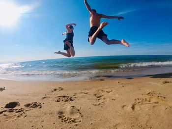 People jumping on beach against sky