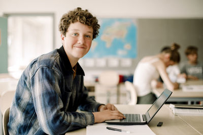 Portrait of teenage boy using laptop while sitting in classroom