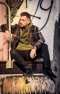 Young man looking down while sitting against wall