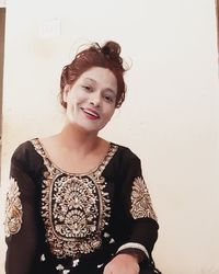 Portrait of smiling young woman standing against wall