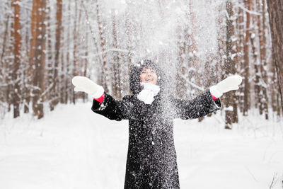 Smiling woman throwing snow mid air during winter