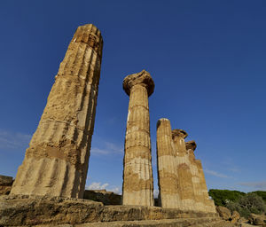 Low angle view of ruins of old greek temple against blue sky