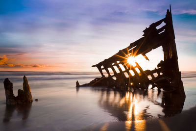 Silhouette wooden posts on beach against sky during sunset