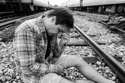 Side view of young man sitting on railroad track