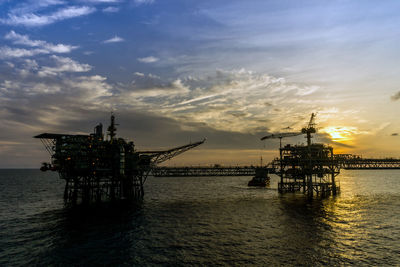 Cranes in sea against sky during sunset