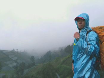 Portrait of hiker wearing raincoat against sky