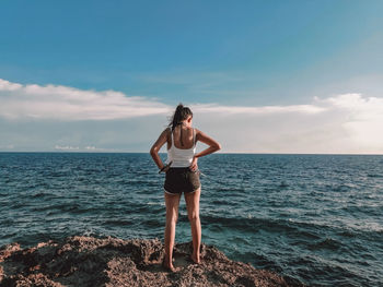 Rear view of woman standing on cliff by sea