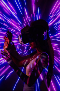 Side view of female exploring virtual reality in modern headset while standing in pink and blue projector lights