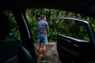 Rear view of woman standing by car against trees
