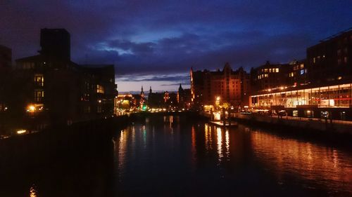 Illuminated city by calm river at night