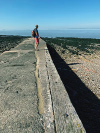 Side view of man standing on retaining wall against clear blue sky