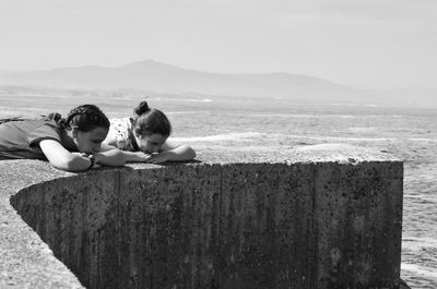 Friends leaning on wall by sea against sky