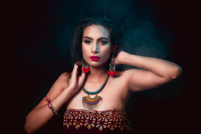 Portrait of young woman wearing jewelry against black background