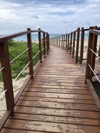 Empty boardwalk leading to sea against sky