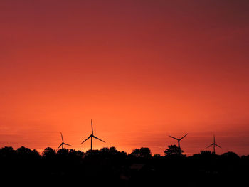 Silhouette windmill on landscape against orange sky