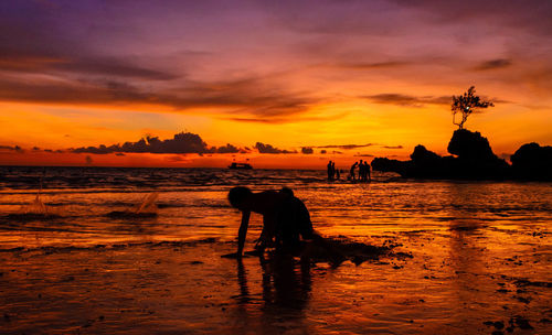 Silhouette people on beach against sky during sunset