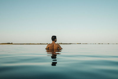 Rear view of man swimming in infinity pool against clear sky