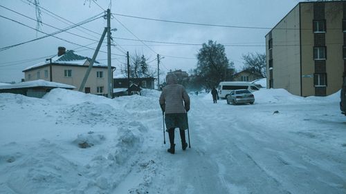 Rear view of man walking on snow covered buildings