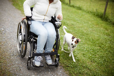 Low section of disabled woman in wheelchair with dog on dirt road