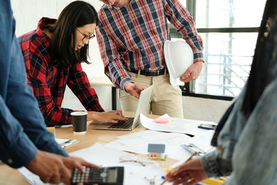 Midsection of architect discussing with woman over laptop in office