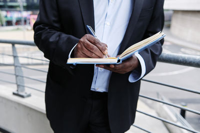 Businessman writing in diary while leaning on railing