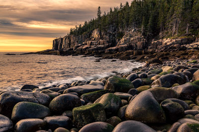 Rocks on beach against sky during sunset