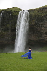 Beautiful woman standing by waterfall against sky