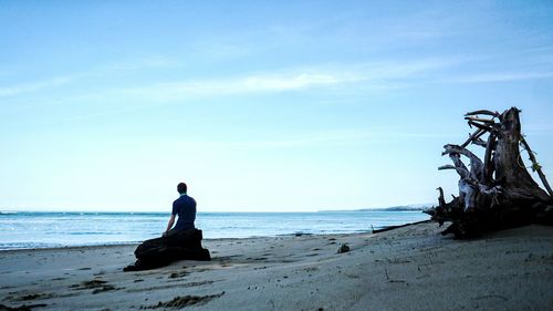 Man sitting on beach against sky